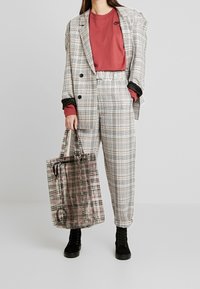 Rutig kostym i grått och vitt med svarta accenter, tillsammans med en röd skjorta och svarta stövlar. Inkluderar en genomskinlig tote-väska med rutigt mönster.