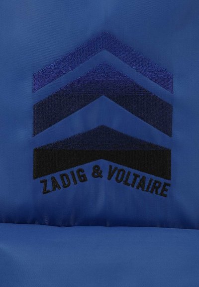 Un tissu bleu avec une texture lisse présente un motif en chevron noir et bleu, accompagné du nom de marque brodé "ZADIG & VOLTAIRE."