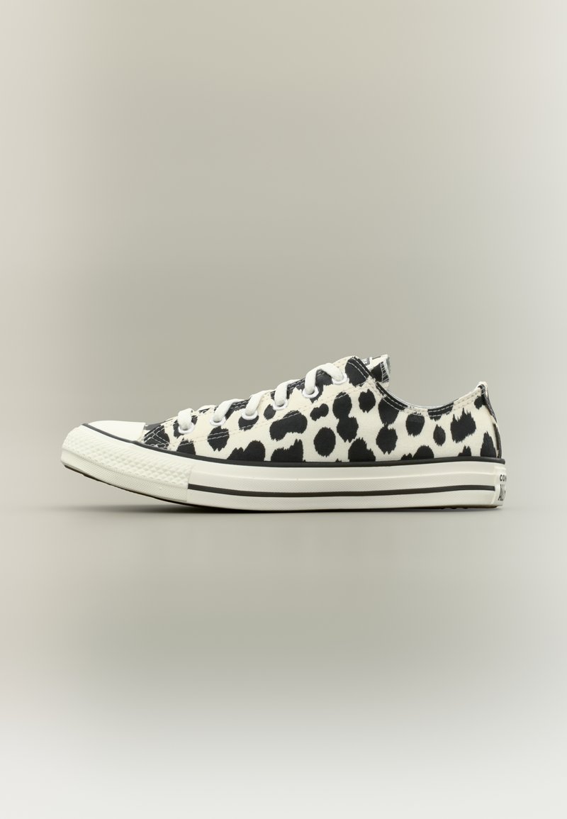 Χαμηλό καμβά παπούτσι με μοτίβο σε μαύρο και λευκό πουά, λευκή λαστιχένια μύτη και λευκά κορδόνια, πάνω σε απλό φόντο.