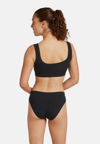 Top de bikini negro con relieve, con tirantes anchos y espalda en forma de scoop, acompañado de braguitas de bikini de talle bajo a juego. Textura suave, diseño minimalista.