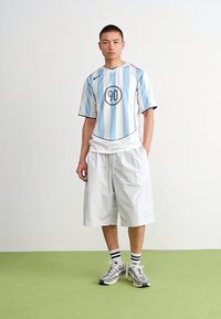 Hvitt og lyseblått stripete kortermet skjorte med et rundt logo, kombinert med hvite shorts. Grå joggesko og svarte stripete sokker.