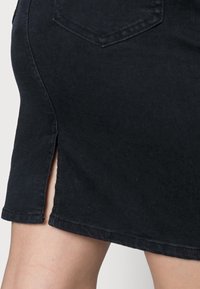 Falda de denim negro con una abertura lateral, costura en el dobladillo y un bolsillo trasero. La tela es suave con un ligero brillo.