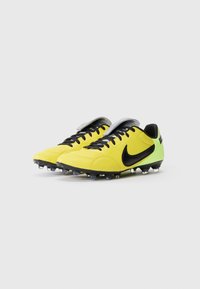 Botas de fútbol amarillas con acentos negros, material sintético texturizado, diseño elegante, cordones negros y una lengüeta plateada. Clavos de goma en la suela.