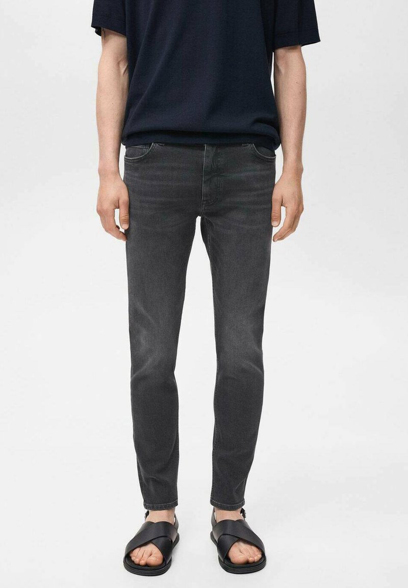 Jeans negros de corte slim con un ligero desgaste, diseño de cinco bolsillos y un detalle de costura mínimo, combinados con sandalias planas negras.