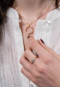 Gold-tone necklace with circular pendant, embellished with small gemstones. Matching gold-tone ring featuring a central blue flower design.