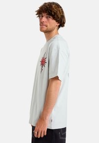 Light gray short-sleeve t-shirt features a red sun graphic on the left chest and side slits at the hem for added detail. Smooth cotton texture.