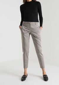 Světle šedé kalhoty na míru s úzkým střihem a sklady, zkombinované s upnutým černým topem s dlouhým rukávem a černými mokasíny.