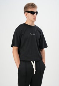 Tricou scurt negru cu mânecă, având un logo alb pe față, asortat cu pantaloni negri cu un șnur de culoare albă. Ochelari de soare negri, lucioși.