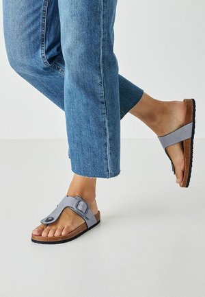 Gray rubber sandals with a footbed made of cork, featuring an adjustable strap and a textured sole, paired with cropped blue denim jeans.