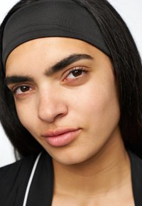 Fascia nera di tessuto indossata su capelli lisci, primo piano del viso che mostra una pelle liscia, trucco naturale e sopracciglia definite.
