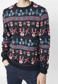 Marinblå stickad tröja med festliga mönster av snögubbar, snöflingor, träd, polkagrisar och renar i röd, blå och vit.