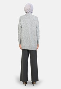 Lys grå strikket sweater med kabelstrik detalje, oversized pasform og ribbet kant, parret med brede grå bukser og hæle.