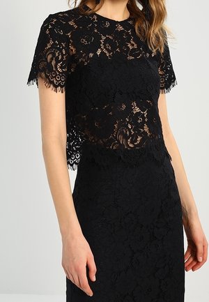 Czarny krótki top z kwiatowej koronki z krótkim rękawem i falistymi brzegami, noszony na dopasowanej, czarnej koronkowej spódnicy z wysokim stanem.