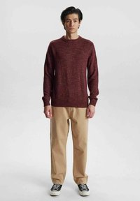 Bordeaux gebreid trui met een ronde hals, gestructureerde stof, lange mouwen; gecombineerd met beige broeken en zwarte sneakers.