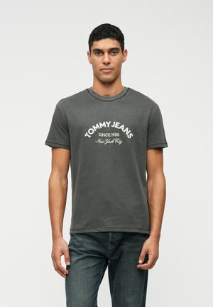Siva bombažna majica z okroglim izrezom, kratkimi rokavi in logotipom "TOMMY JEANS" ter besedilom "SINCE 1985" in "New York City" v beli barvi.