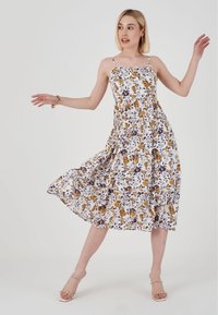 Bloemen midi-jurk met dunne bandjes; witte achtergrond met gele en paarse bloemen; vloeiende rok met een getailleerde taille; lichte stof.