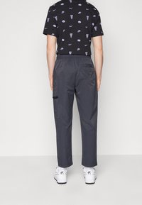 Schwarzes gemustertes T-Shirt mit Nike-Logos, kombiniert mit grauen Cargo-Hosen mit elastischem Bund, seitlichen Taschen und kontrastierenden Beschlägen.