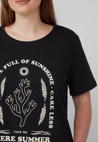 Zwarte katoenen t-shirt met een witte graphic van een zon, koraalontwerp en tekst: "VOL MET ZONNESCHIJN • MAKEN JE MINDER ZORGEN • NEEM ME MEE NAAR DE ZOMER."