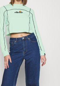 Ljusgrön kortärmad topp med svarta detaljer och en 'ellesse'-logotyp. Bärs med hög midja mörkblå denimjeans.