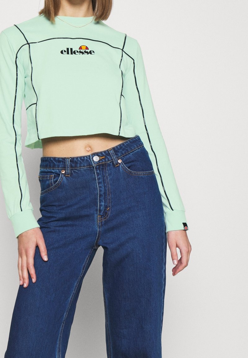 Ljusgrön kortärmad topp med svarta detaljer och en 'ellesse'-logotyp. Bärs med hög midja mörkblå denimjeans.