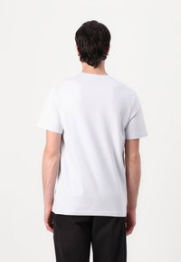 Vit kortärmad t-shirt med rund halsringning och mjuk bomullstextur, bärs med mörka byxor, visad från bakperspektiv.