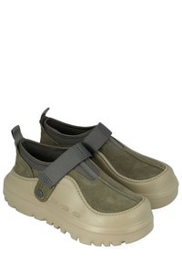 Scarpe slip-on con suola beige spessa, tomaia in camoscio verde oliva e ampie fasce elastiche grigie sul collo del piede.