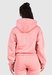 Sudadera rosa con un corte relajado, que cuenta con una gran capucha y puños acanalados. Hecha de un material suave y texturizado, combinada con pantalones a juego.