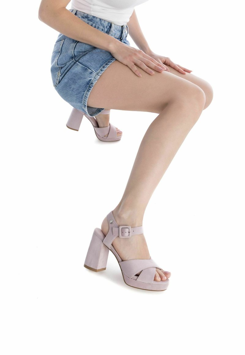 Sandalias de tacón alto en un rosa claro, con una correa ancha y hebilla, que presentan una superficie texturizada y un tacón grueso.