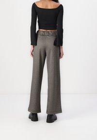 Zwarte lange mouwen top met uitlopende manchetten, gecombineerd met wijde broek in een geruite stof. De broek heeft een elastische tailleband en zakken.