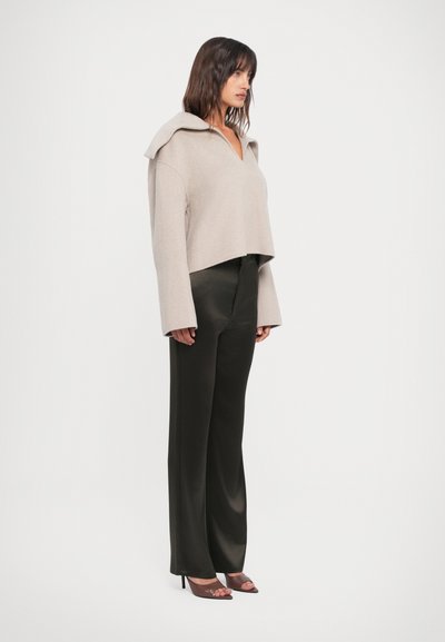 Bežist villane segu cropped-sweater V-kaelusega ning üleulatuva kraega; koos kõrge vöökohtadega, läikivate mustade laienevate pükstega ja avatud varbaga kontsadega.