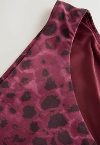 Close-up of a maroon fabric with dark purple irregular spots and stitching detail on a sleeveless garment.