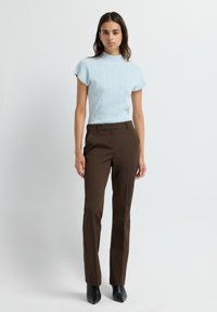 Haut tricot à manches courtes bleu clair avec col montant, associé à un pantalon beige ajusté et des escarpins noirs à bout pointu. Design texturé uni.