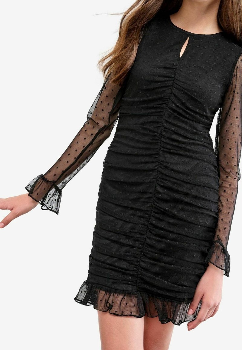 Mini-robe noire froncée avec manches longues transparentes à pois et ourlet à volants, avec petit détail découpé à l'avant.