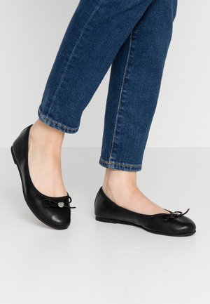 Schwarze Leder-Balletschuhe mit runder Spitze, dekorativem Schal und kleinem metallischen Akzent. Getragen mit verkürzten blauen Jeans.