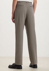 Pantaloni a motivo pied de poule in nero e beige, con vestibilità dritta, vita su misura e tasche posteriori. Abbinati a scarpe nere.