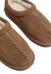 Brown suede slippers with white plush lining and decorative white stitching along the top center seam.