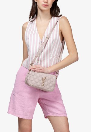 Donna che indossa un gilet senza maniche a righe rosa e bianche e pantaloncini rosa, con una borsa a tracolla beige trapuntata con logo V73 dorato.