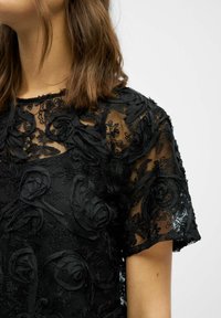 Sort gennemsigtig bluse med tekstureret blomsterbroderi, korte ærmer og rund halsudskæring. Stoffet har et fint og lagdelt udseende.