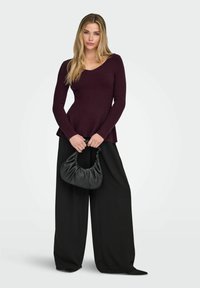 Top bordeaux a maniche lunghe a coste con scollo a V, abbinato a pantaloni neri larghi e una piccola borsa nera arricciata. Texture liscia.