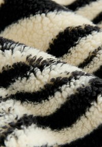 Schwarz-weiß gestreifte Plüschdecke mit einer weichen, flauschigen Textur und einem gewellten Design, das verschiedene Längen und Tiefen des Stoffs aufweist.