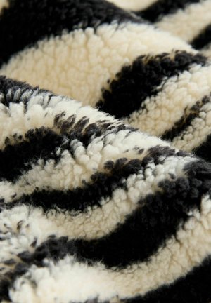 Coperta plush a righe nere e crema con una consistenza morbida e soffice e un design ondulato, caratterizzata da lunghezze e profondità variabili del tessuto.