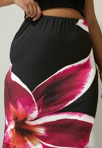 Svart kjol med ett stort, livligt blommönster i rosa och vitt. Mjukt, stretchigt tyg med elastisk midja för en åtsittande look.
