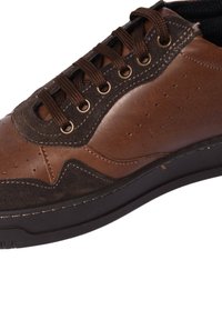 Sneaker in pelle e suede marrone con punta arrotondata, texture contrastanti e occhielli in metallo. Caratterizzato da una suola in gomma scura e delicate perforazioni.