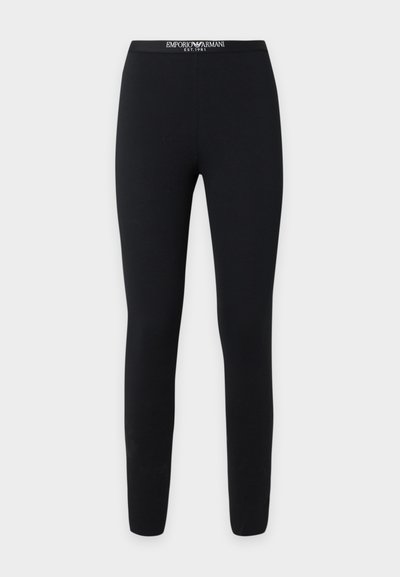Leggings noirs ajustés avec un texte blanc sur la ceinture de marque Emporio Armani, affichant le logo et "EST. 1981" sur un fond uni.