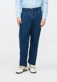 Tumesinised sinisest teksast püksid lahtise lõikega, esiküljel voltidega, nupuga kinnine ja mitme vööaasaga. Kandmiseks sobivad heledad tossud.