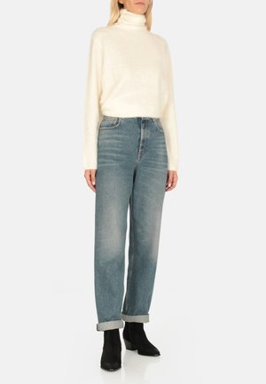 Maglione a collo alto crema in morbido e peloso tessuto abbinato a jeans azzurri chiari a vita alta, con orlo risvoltato alla caviglia, completato da stivali con tacco neri.