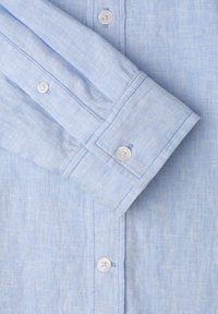 Chemise en lin bleu clair à manches longues avec boutons blancs, bouton de manchette fermé et texture tissée subtile.