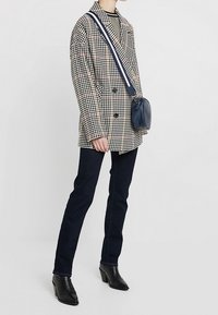 Dvoubreasted sako se vzorem pepito v černé a krémové barvě, doplněné tmavými džínami a černými botami na podpatku. Součástí je malá modrá kabelka přes rameno.