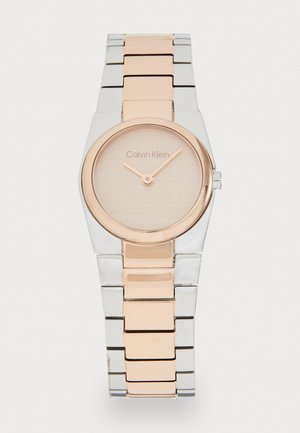 Montre en métal argenté et rose doré avec un cadran rond, au design minimaliste et un cadran texturé de couleur claire. Elle présente un bracelet à maillons élégant.