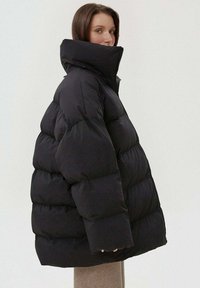 Černá péřová bunda s vysokým límcem a oversized siluetou. Vyrobena z hladkého, polstrovaného materiálu, s zipovým zapínáním a širokými manžetami.